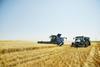 Combine harvestor and tractor driving through field of arable crops