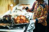 woman basting turkey on top of oven