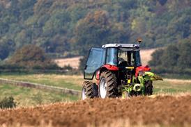 Tractor ploughing a field with a forest in the distance