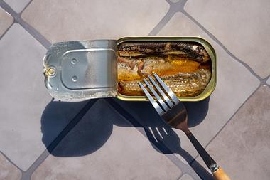 Overhead view of open sardine tin with a fork inside, casting long shadows on a tiled surface. Simple food or emergency meal. - stock photo