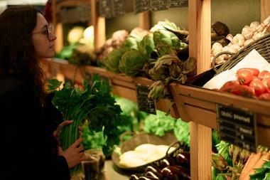 Woman selecting fresh vegetables at a market stall filled with diverse produce - stock photo - Getty Images