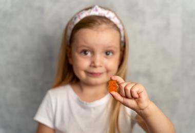 A child holding a supplement in the shape of a gummy bear