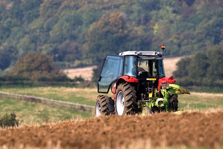 Tractor ploughing a field with a forest in the distance