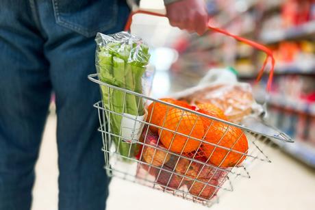 Man holding shopping basket containing leeks and oranges