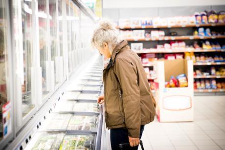 Mature woman in supermarket, looking in freezer cabinet - stock photo
