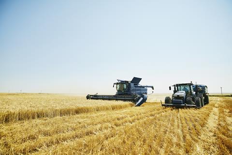 Combine harvestor and tractor driving through field of arable crops