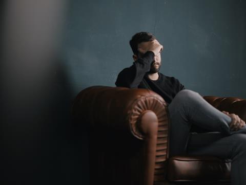 man sitting on a sofa with head in hand mental health depression sad