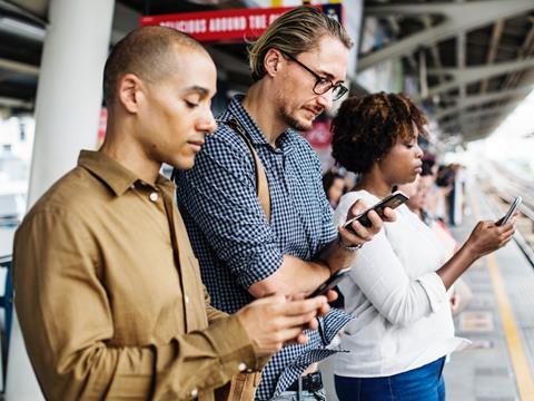 Three people at a train station staring at their mobile phones_digital