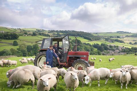 Farmer in tractor with son watching sheep in field - Getty Images