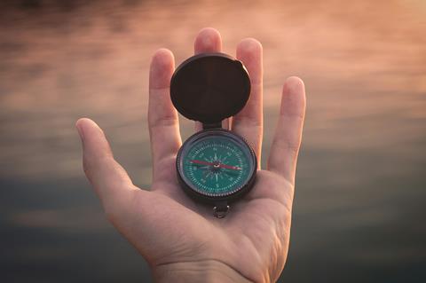 a hand holding an open compass, with the sea in the background