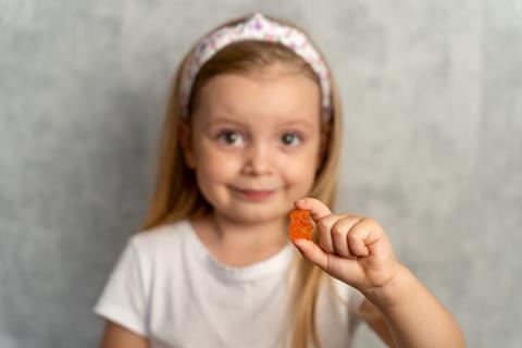 A child holding a supplement in the shape of a gummy bear